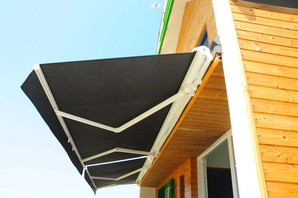 Terrasse ext&eacute;rieure avec store banne d&eacute;ploy&eacute; sous ciel bleu