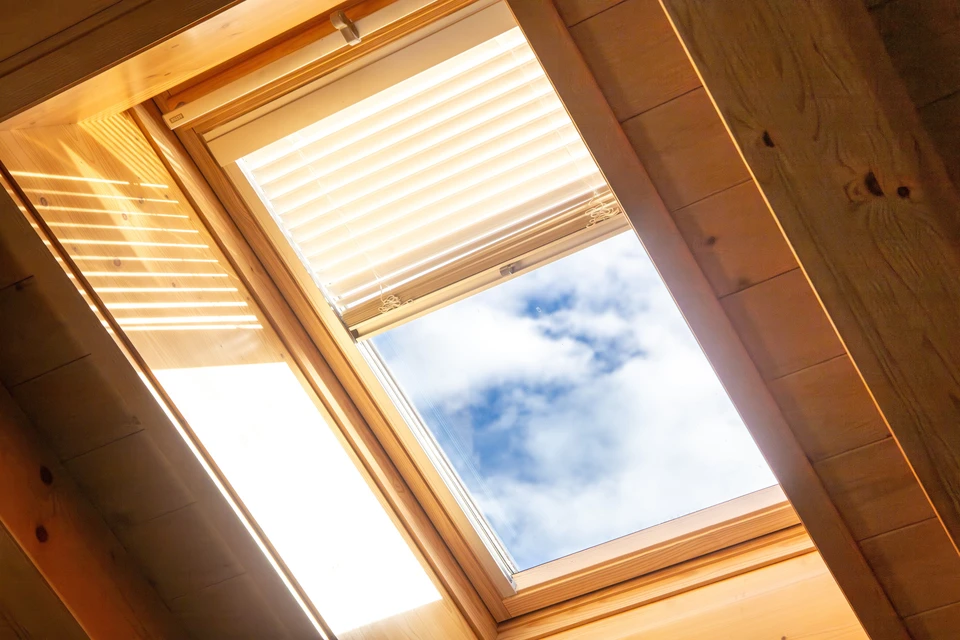 Intérieur d'une habitation sous combles avec vue sur le ciel nuageux à travers une fenêtre de toit ouverte