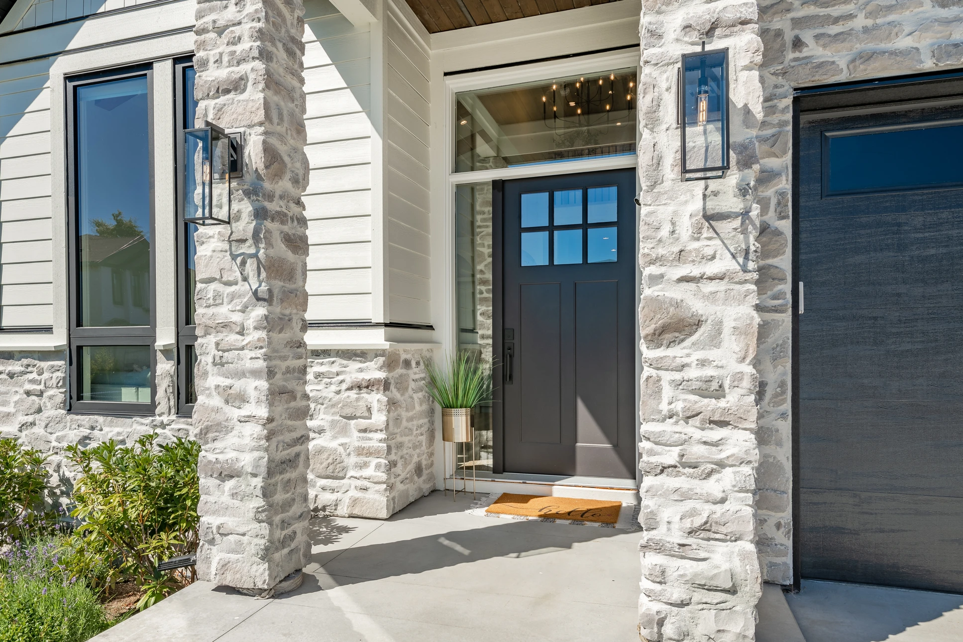 Entrée principale d'une maison contemporaine avec porte d'entrée noire à panneaux vitrés, encadrée par des colonnes en pierre naturelle blanche
