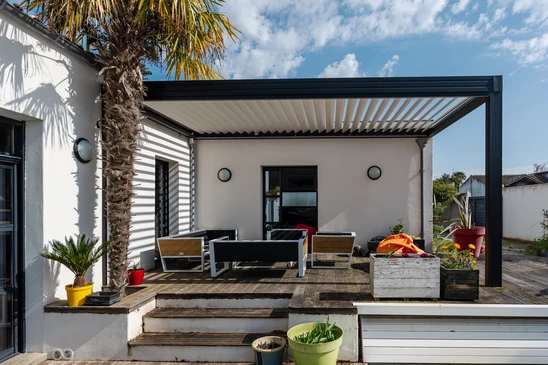 Terrasse ext&eacute;rieure moderne avec pergola bioclimatique &agrave; lames orientables, mobilier de jardin contemporain sur plancher bois