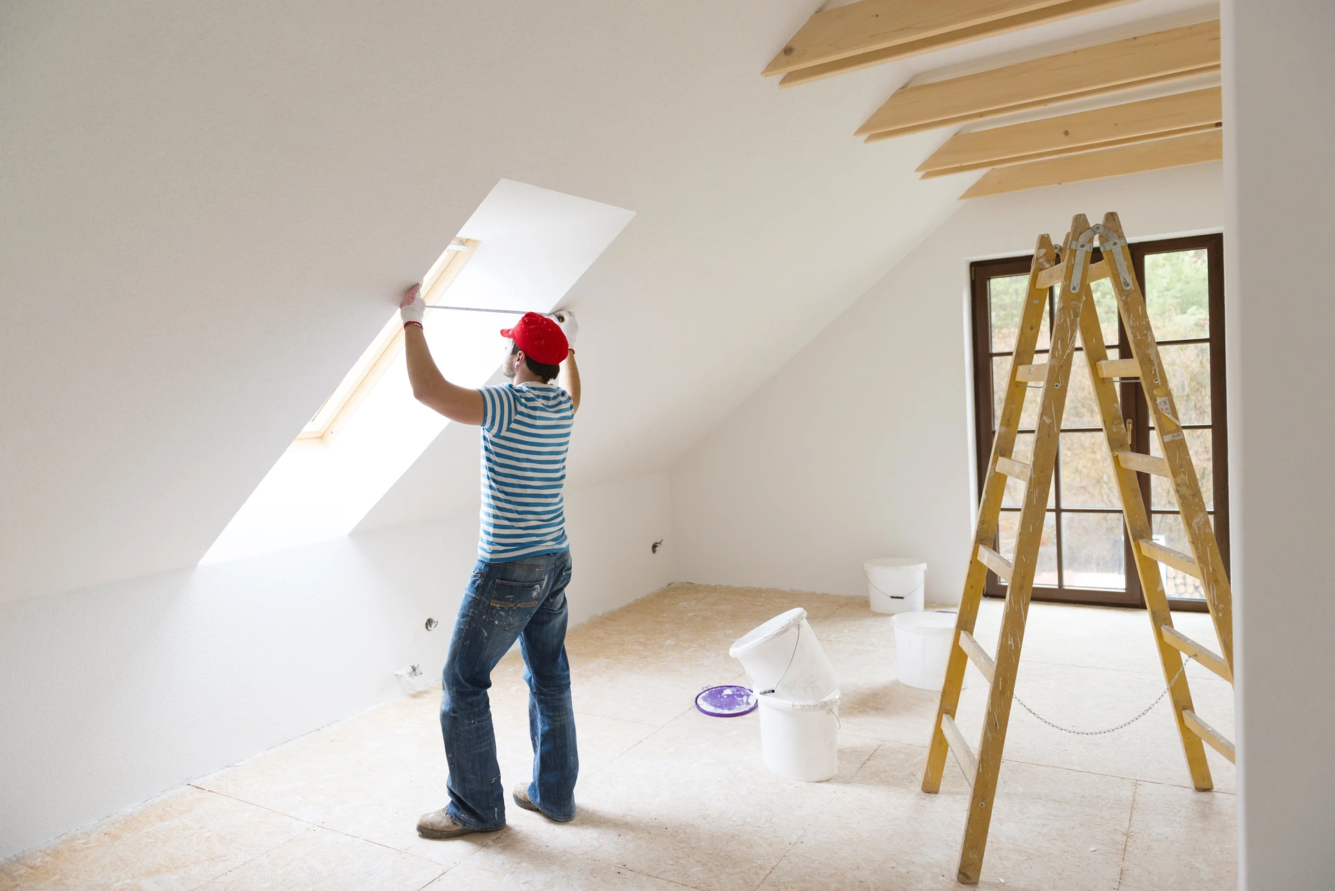 Artisan installateur en tenue de travail bleue et casquette blanche manipule une fenêtre à double vitrage dans un intérieur résidentiel