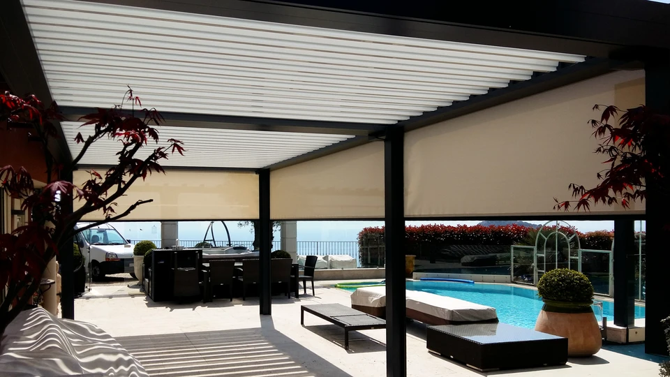Terrasse couverte moderne avec pergola bioclimatique à lames orientables noires, mobilier d'extérieur gris contemporain, vue sur villa en pierre naturelle et végétation méditerranéenne