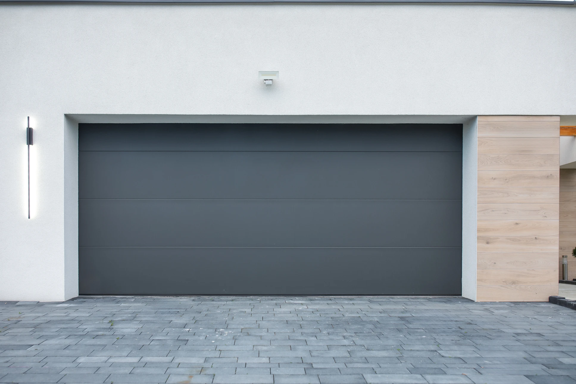 Deux techniciens en combinaisons de travail et casques orange installent une porte de garage sectionnelle blanche dans un garage résidentiel